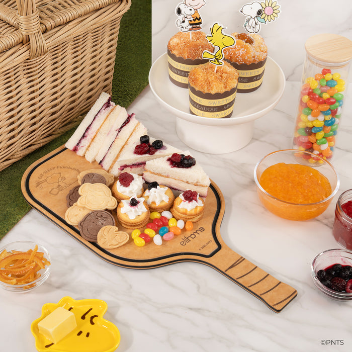 Wooden platter with assorted finger foods, including sandwiches and pastries, on a white surface.