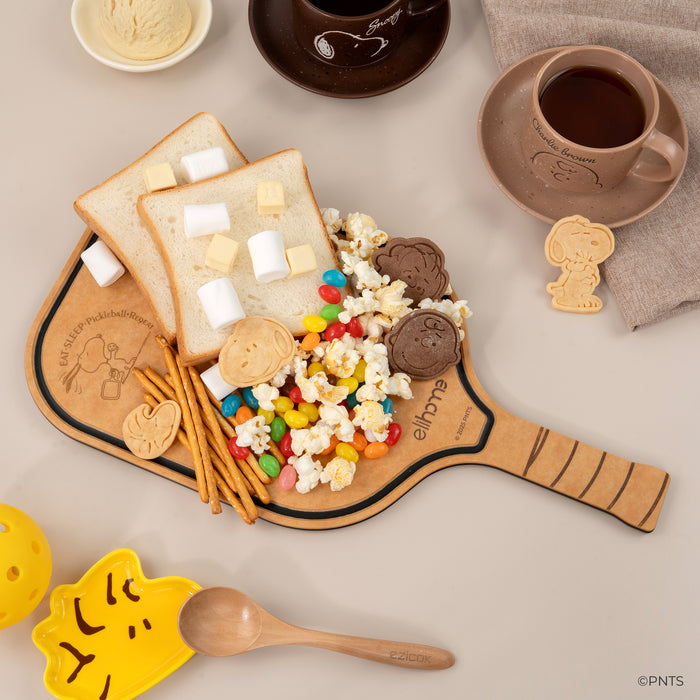 Wooden paddle with snacks including cookies, popcorn, and candy on a neutral background.