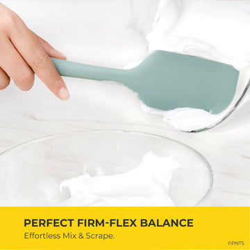 Silicone spatula being used to mix a white substance in a clear bowl with text about firm-flex balance.