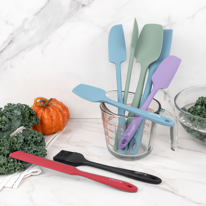Elihome silicone spatulas and spoonulas in Teal Grey, Sage Green, Purple, Tiffany Blue, Red and Black in a glass measuring cup on a marble counter with kale and a pumpkin