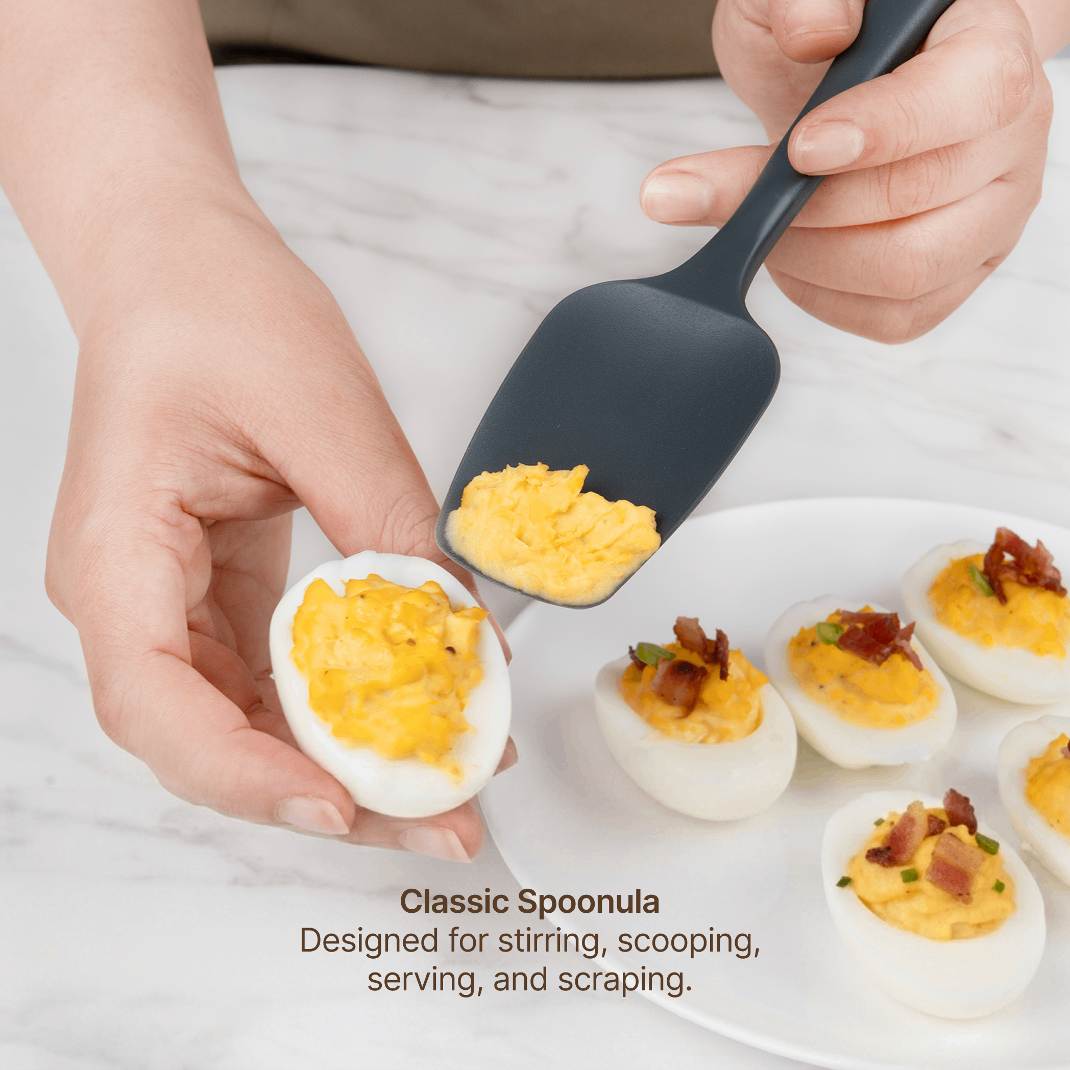 Hand using the Elihome x Peanuts Classic Spoonula to scoop filling onto deviled eggs, designed for stirring, scooping, serving and scraping
