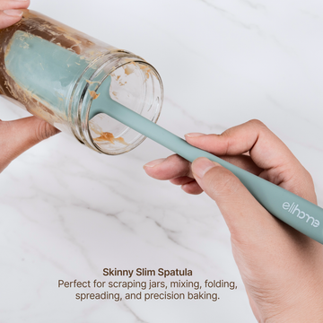 Hands using the Elihome x Peanuts Skinny Spatula to scrape the inside of a glass jar, perfect for scraping jars, mixing, folding, spreading and precision baking