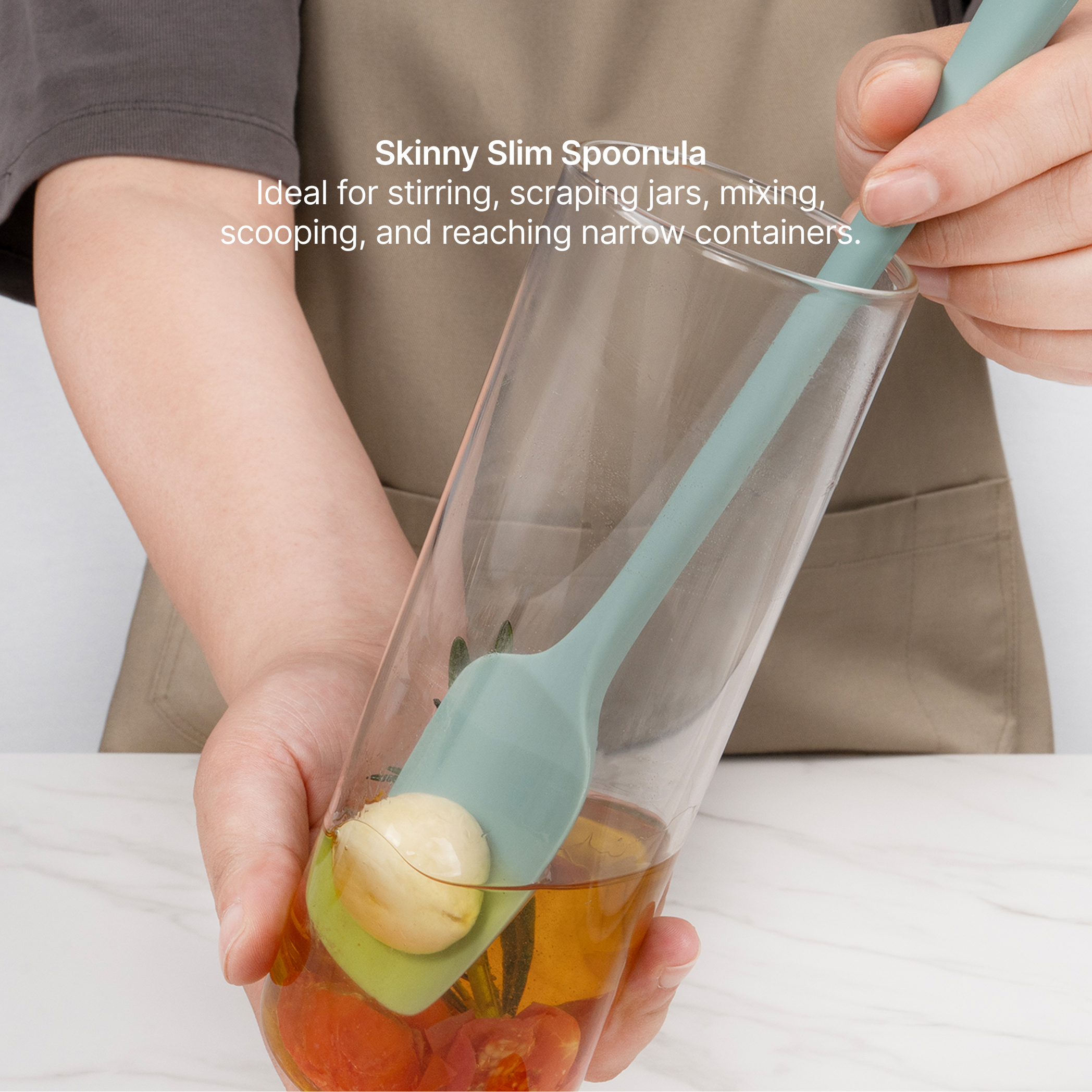 Hand using the Elihome x Peanuts Skinny Spoonula to reach fruit at the bottom of a tall glass, ideal for stirring, scraping jars, mixing, scooping and reaching narrow containers