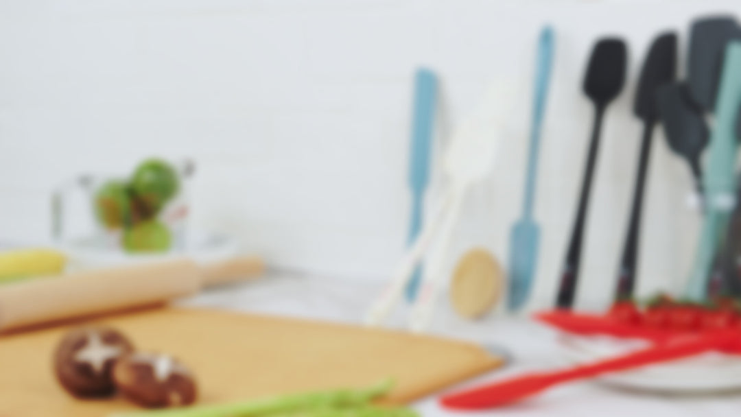 Video frame displaying the Elihome Sage Green silicone utensil set components. Labels identify the Mini Basting Brush, Classic Spoonula, and Skinny Spoonula arranged on a marble counter.