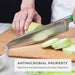 Hand slicing zucchini on an antimicrobial fiber wood cutting board, highlighting the non-porous surface that is safe from harmful bacteria and infections.